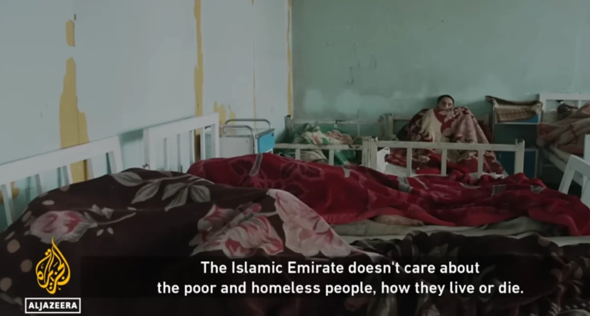 People wrapped in blankets lie on beds in a bare, dilapidated room, with Al Jazeera branding in the corner and a subtitle that reads, "The Islamic Emirate doesn't care about the poor and homeless people, how they live or die."