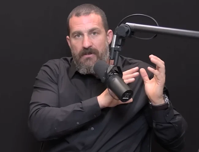 Dr. Andrew Huberman Dr. Andrew Huberman, a bearded man in a black shirt, speaks into a black microphone against a dark background.
