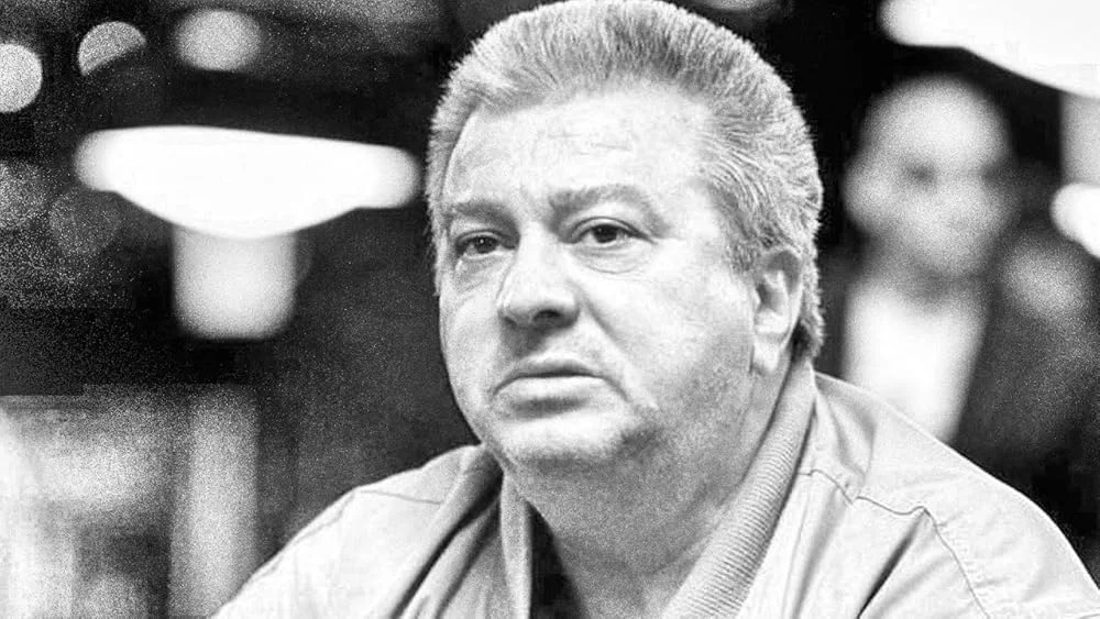 Black and white photo of Archie Karas in what appears to be a poker room.