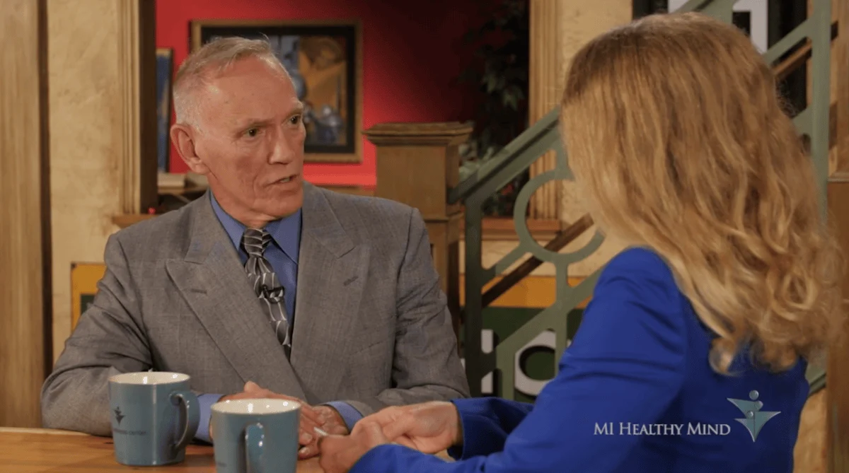 Michael Mooney and a woman with blonde hair seated at a table, discussing his gambling addiction during an interview.