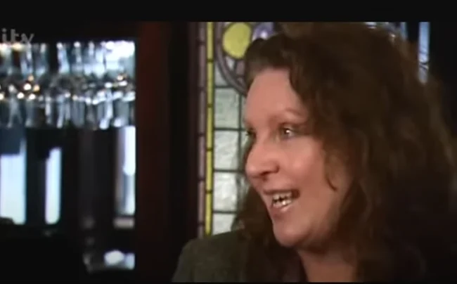 Jane Peyton, a woman with long hair, is engaged in conversation with another person.