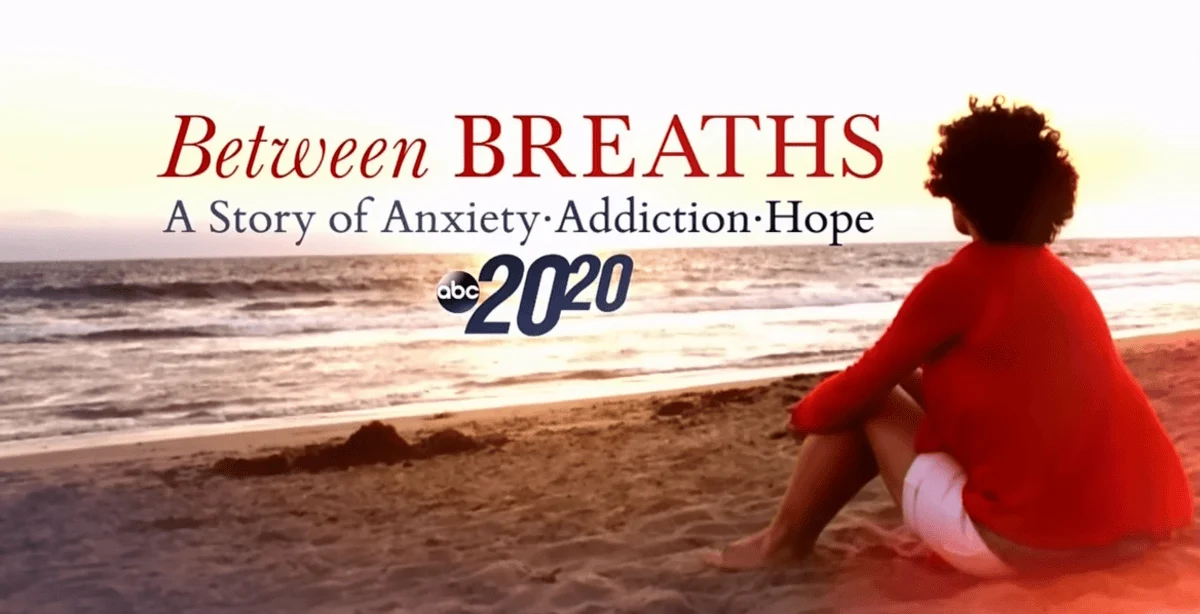 Elizabeth Vargas sits on the beach at sunset in a red sweater, gazing at the ocean. Text reads, "Between Breaths: A Story of Anxiety, Addiction, Hope. ABC 2020."