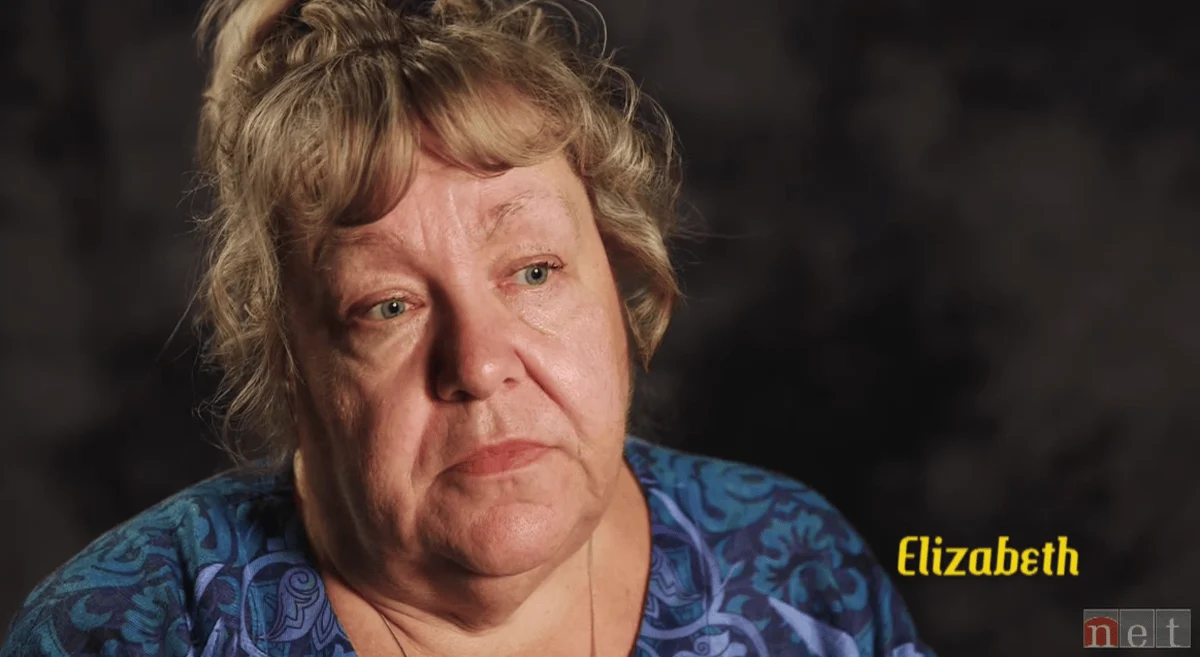 An older woman with short, wavy hair looks contemplative against a dark background. She wears a blue patterned top. The name "Elizabeth" is written in yellow.