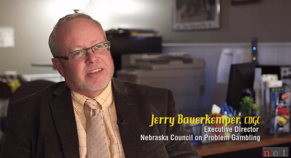 Man in a suit with glasses speaks in an office setting. Yellow text reads "Jerry Bauerkemper, CDGC". White text reads "Executive Director, Nebraska Council on Problem Gambling." The tone is professional.