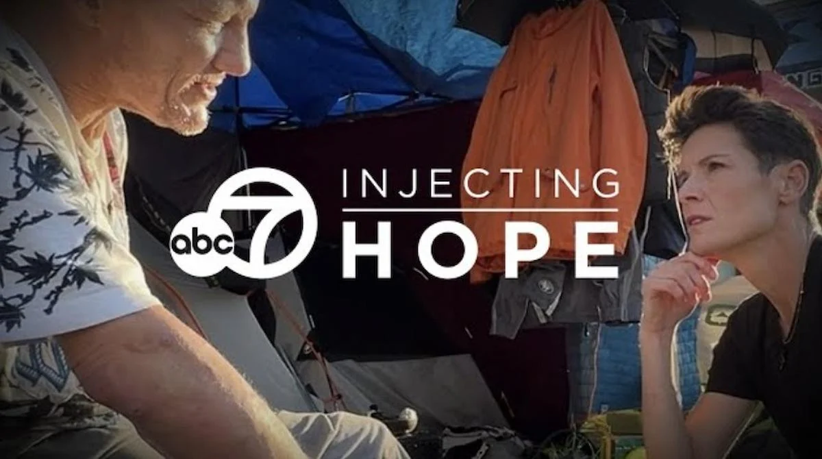 Two people converse earnestly near a tent, suggesting a homeless setting. The "ABC 7 Injecting Hope" logo overlays the scene.