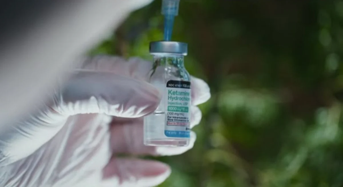 Gloved hands prepare to place a syringe into a small bottle, featured on the cover of Hamilton’s Pharmacopeia Ketamine Realms & Realities