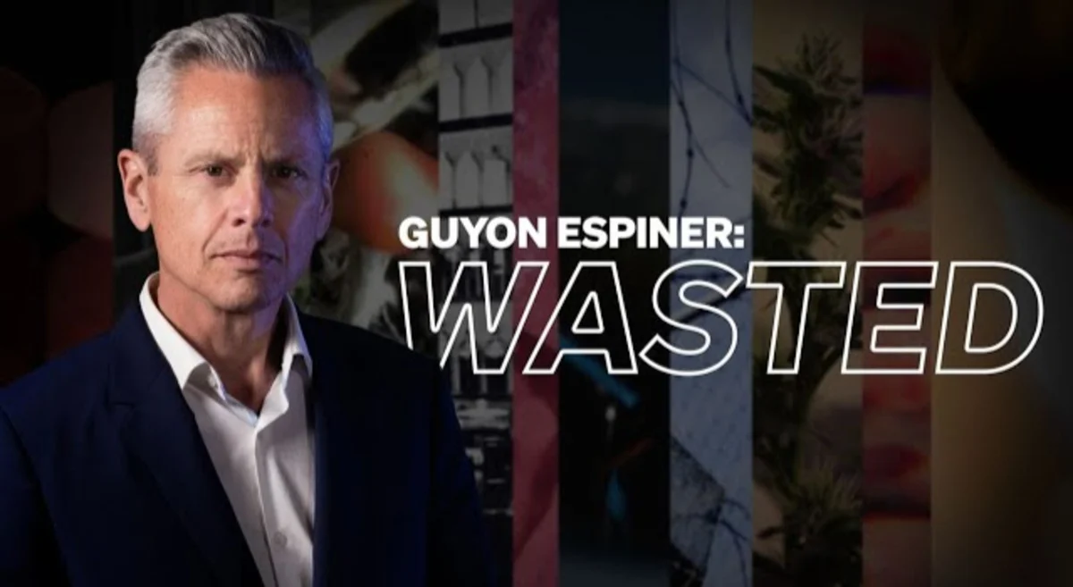 Guyon Espiner dressed in a suit on the left, alongside the title "Guyon Espiner: WASTED" and a collage of background images.