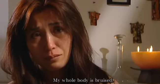 A tearful Minh, Phillip's ex-wife, gazes into the camera with a candle in front of her, highlighting her emotional state.