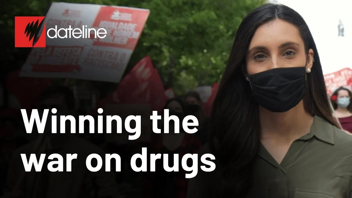 A woman wearing a black mask stands in front of a blurred crowd holding red banners. Text reads "Winning the war on drugs" with Dateline logo.