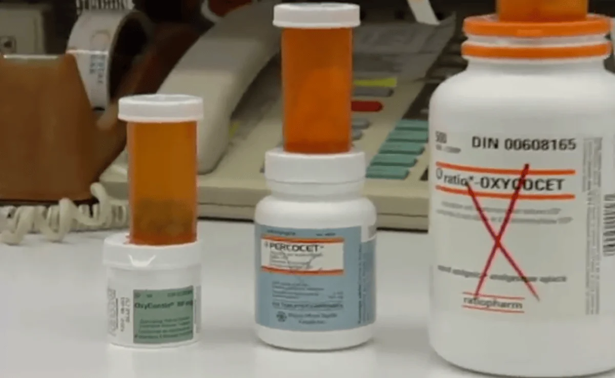 Three prescription pill bottles on a pharmacy counter, featuring labels for different medications, including OxyContin and Percocet, highlighting that these are a prescription for addiction.