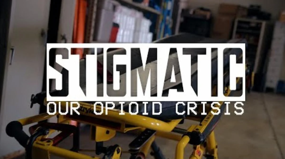 A yellow emergency stretcher in a dimly lit room with shelves. Overlay text reads: 'Stigmatic: Our Opioid Crisis'.