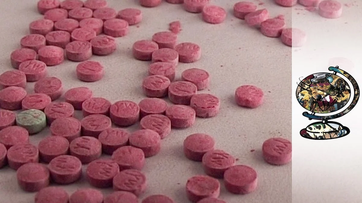 Scattered pink pills with an "M" imprint lay on a flat surface, with a single green pill among them, depicting Thailand's war on drugs. A colorful globe illustration is on the right.
