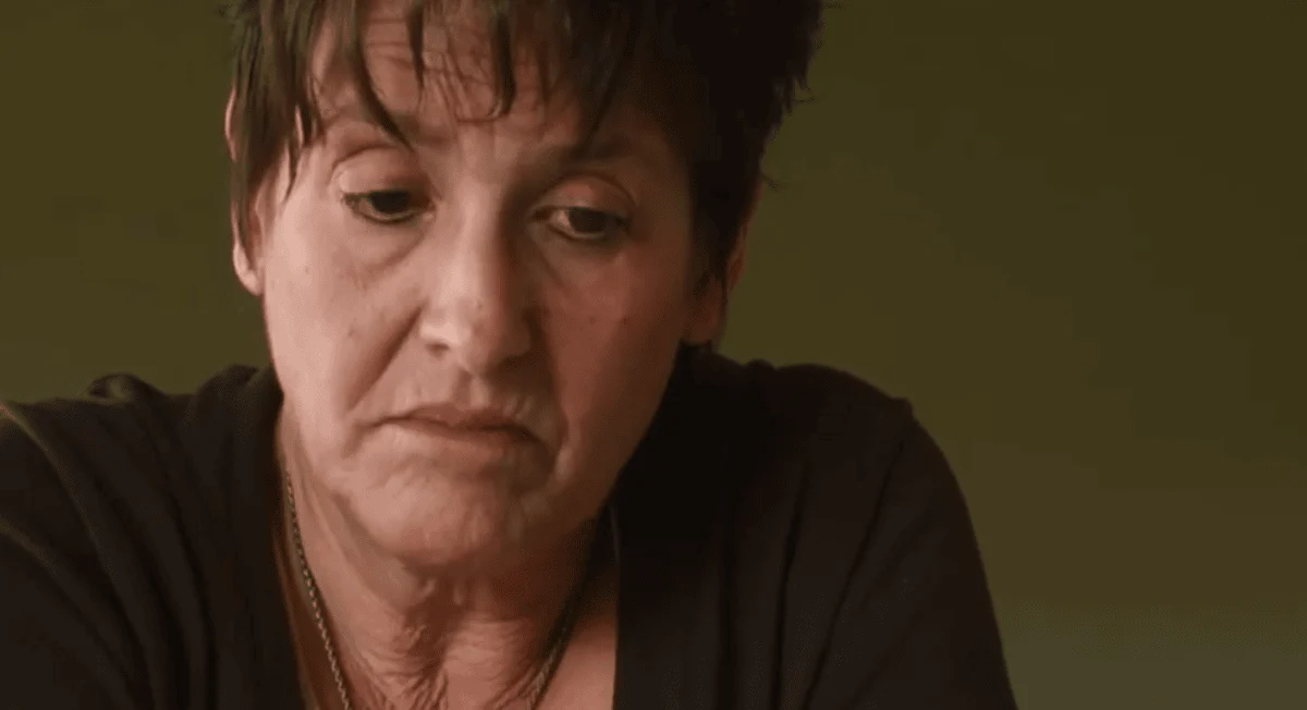 Joy, a woman with short hair, gazes down at the camera in a close-up from Understanding Joy.